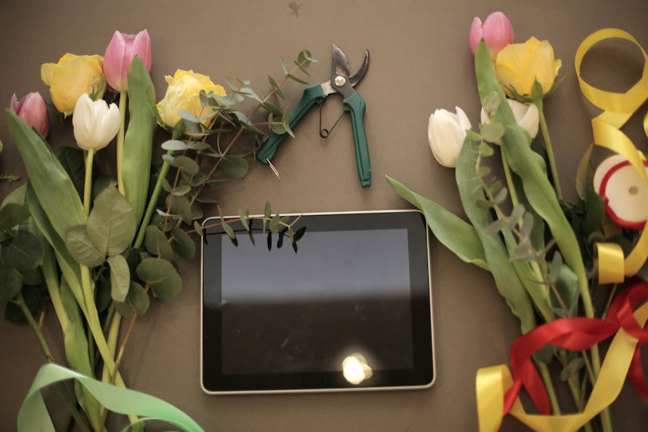 A flat-lay arrangement featuring several bouquets of fresh tulips in soft pastel pink, yellow, and white, with their green leaves and stems visible, laid out on a neutral surface. Among the flowers, t